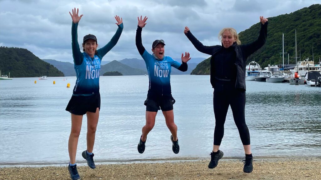 3 Women Jumping in the air with a background of beach and water.